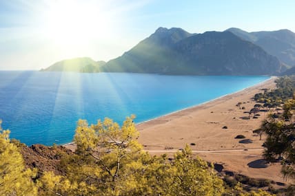 Die Sonne scheint über einen Sandstrand und dem leuchtend blauen Meer bei Cirali.