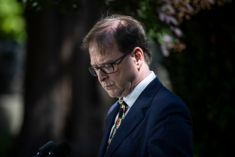 A white man wearing a patterned tie looks down.