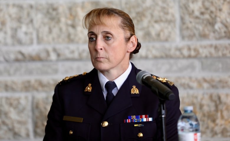 A woman in an RCMP uniform with many medals sits in front of a microphone.