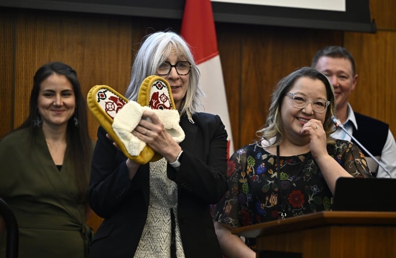 Indigenous Services Minister Patty Hajdu holds up a gift of moccasins from Assembly of First Nations National Chief Cindy Woodhouse.