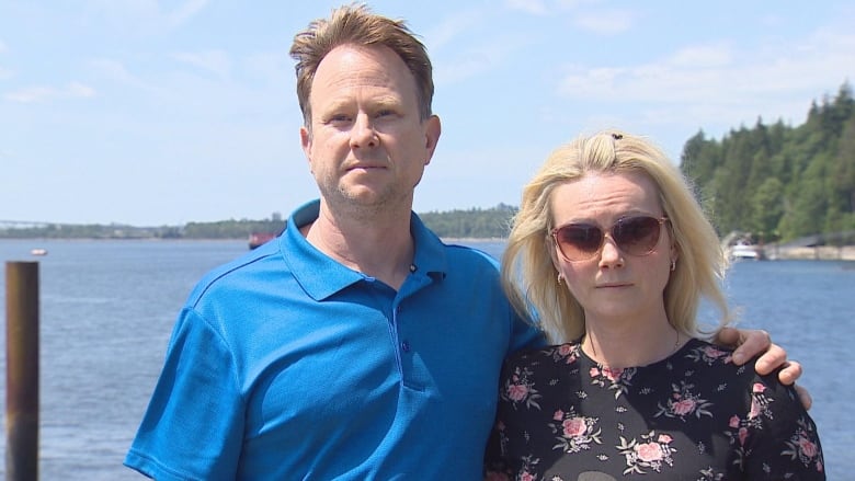 A man and a woman pose for a photo while in front of a large body of water.