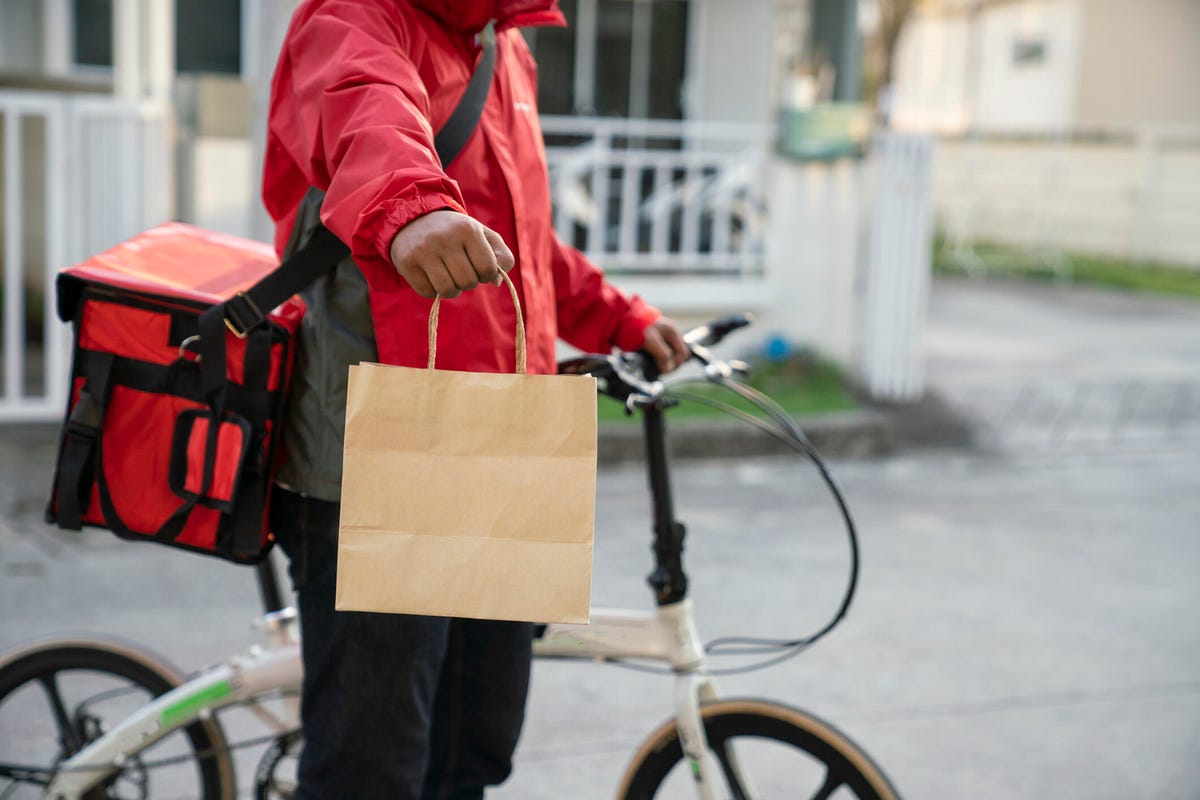 A delivery person on a bicycle holding a brown takeout bag