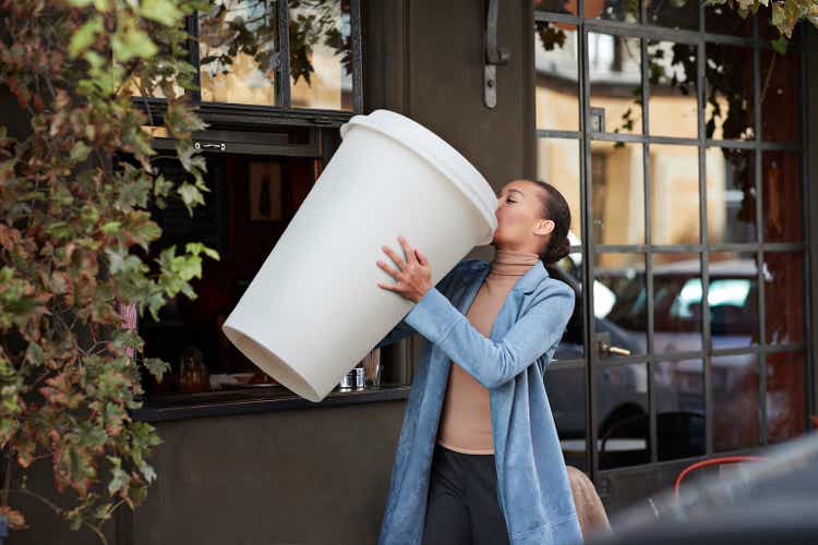 Woman drinking coffee from large disposable cup at take away counter of cafe