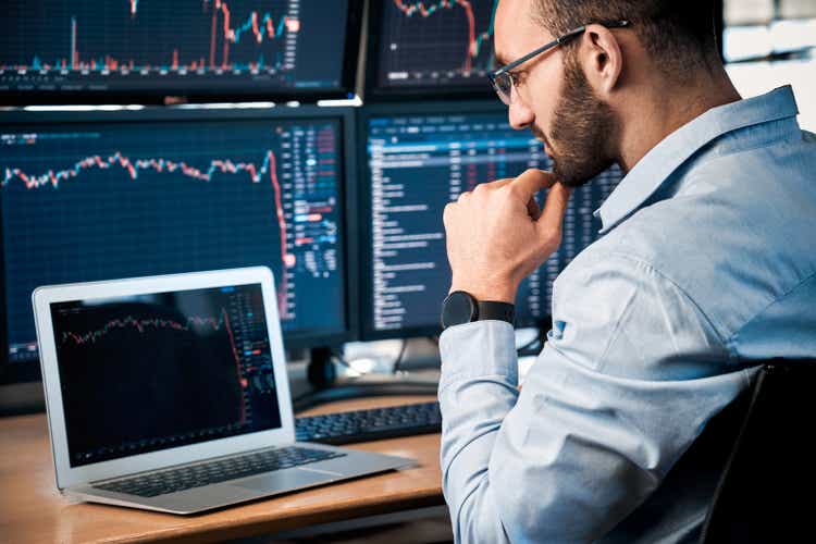 Stock Traiding. Trader sitting at office looking at laptop interpreting candlestick price chart pensive close-up