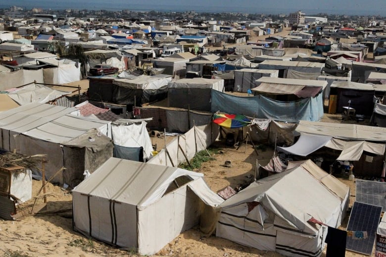 Several tents are shown as far as the camera lens can capture, in an open era with dirt ground.