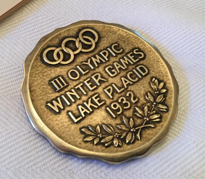 A gold medal on a table that reads "Olympic Winter Games Lake Placid 1932." 