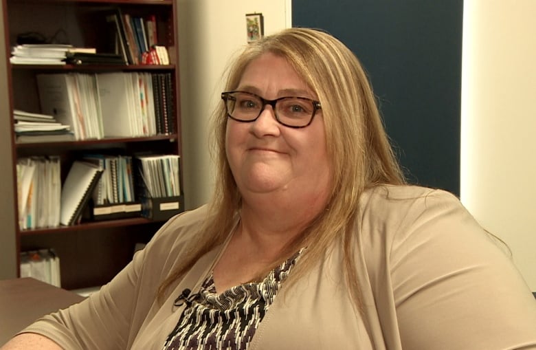 A woman wearing glasses smiles while looking into the camera.