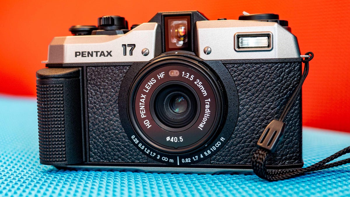 Pentax 17 compact 35mm film camera sitting on a blue couch with a red background.