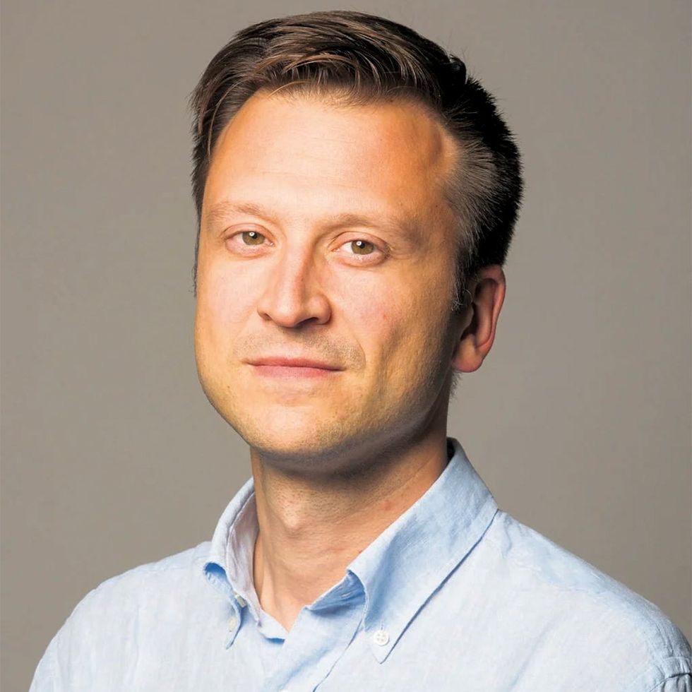 Portrait of a clean-shaven man with brown hair wearing a blue button down shirt.