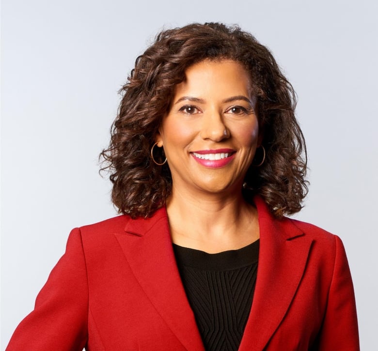 A woman with dark skin aand dark curly hair wearing a red blazer smiles at the camera.  