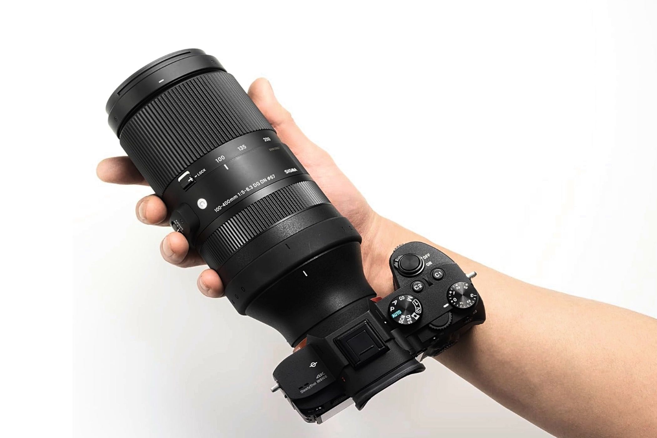 A person's hand holding a Sigma 100-400mm F5-6.3 DG DN OS Contemporary lens mounted onto a camera.