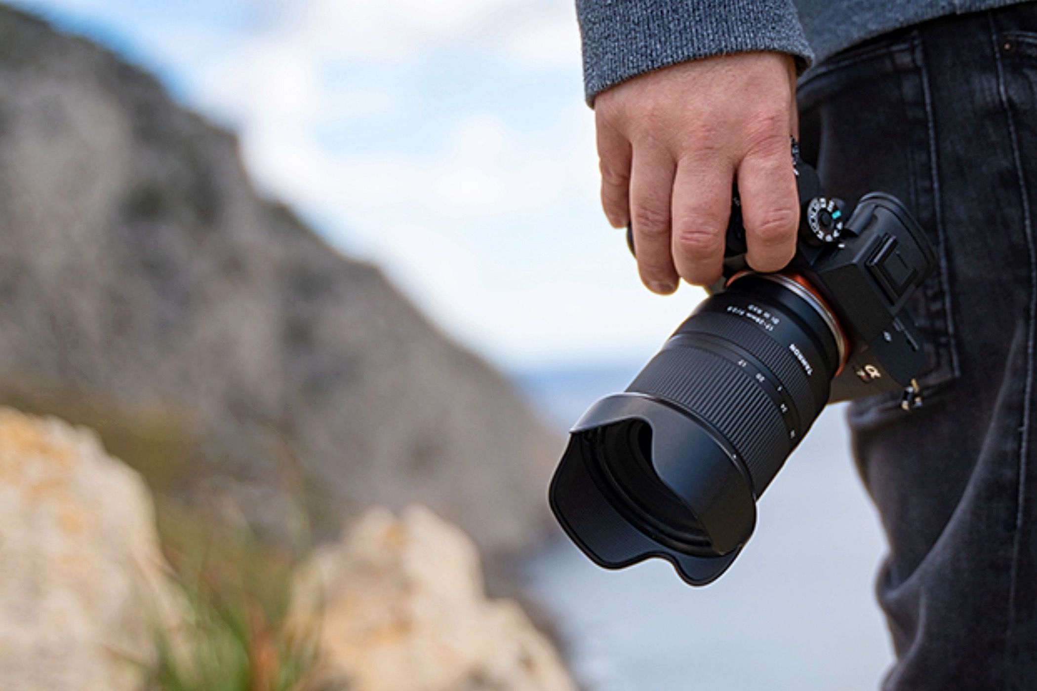 A man holding a camera with a Tamron 17-28mm f2.8 Di III RXD lens attached.