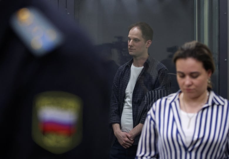 A man stand behind a glass wall of an enclosure for defendants in court.