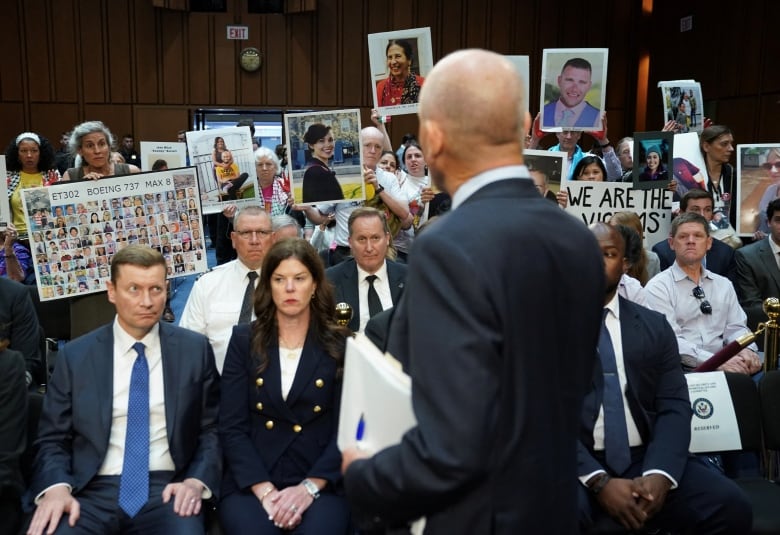 A man faces an audience behind him, some of them holding pictures of relatives.