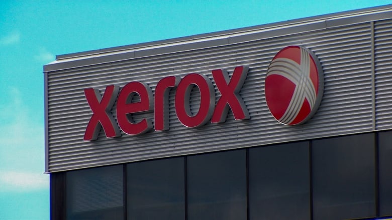 Red lettering and company logo o the top of a grey building.