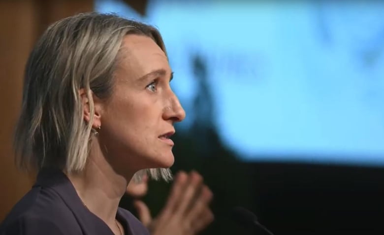 A woman is seen speaking to a crowd from the side